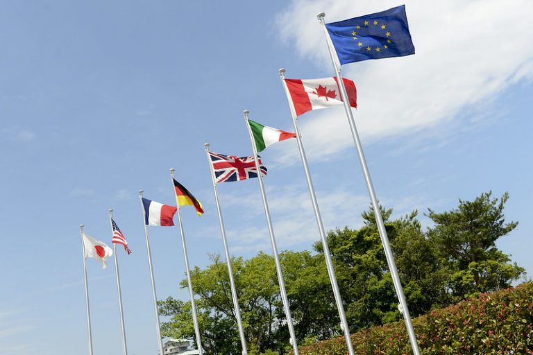 National flags against a blue sky with trees in background.