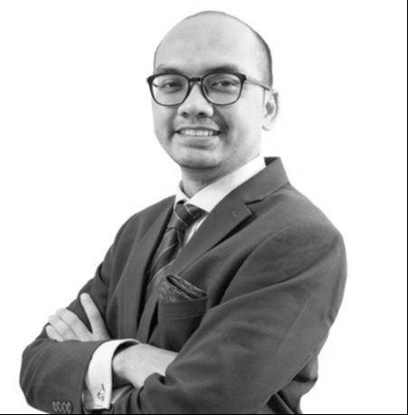 A man in a suit and tie, wearing glasses, stands with his arms crossed, smiling. The image of Ariyo Irhamna is in black and white.