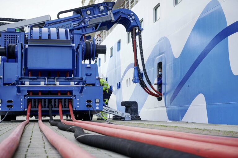 A worker oversees an electric-powered ship charging device that provides shore power to a cruise ship docked at a port.