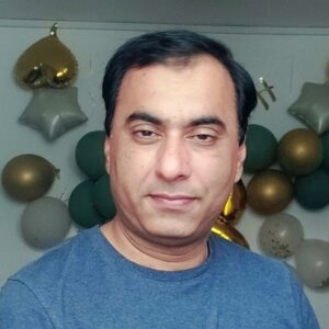 A man in a blue shirt stands in front of a backdrop of gold, white, and green balloons at the Tyndall Spotlight event.