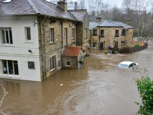 Brown and white concrete houses, The Brown Cow pub, and semi-submerged cars as the River Aire water floods into Bingley, UK on Boxing Day, 2015.