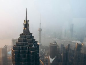 Aerial view of city buildings and stormy sky during daytime in Shanghai, China, with river in background.