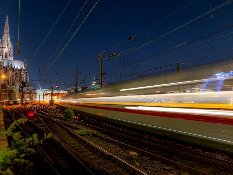 An ICE high-speed train leaving the Cologne Central Station in Europe, at night time, with the cathedral spire in the background.