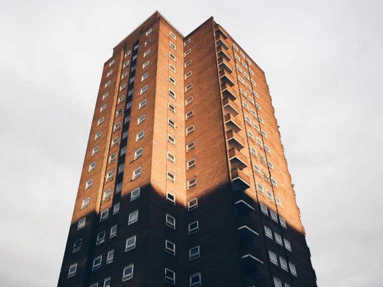 A tall residential apartment building in Brighton, UK, partly in shadow at the top but the top two thirds in direct sunlight - an example of the need for cooling demand in social housing design.