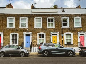 A row of Victorian houses, with colourful front doors, in London, UK, and with cars parked in the front.