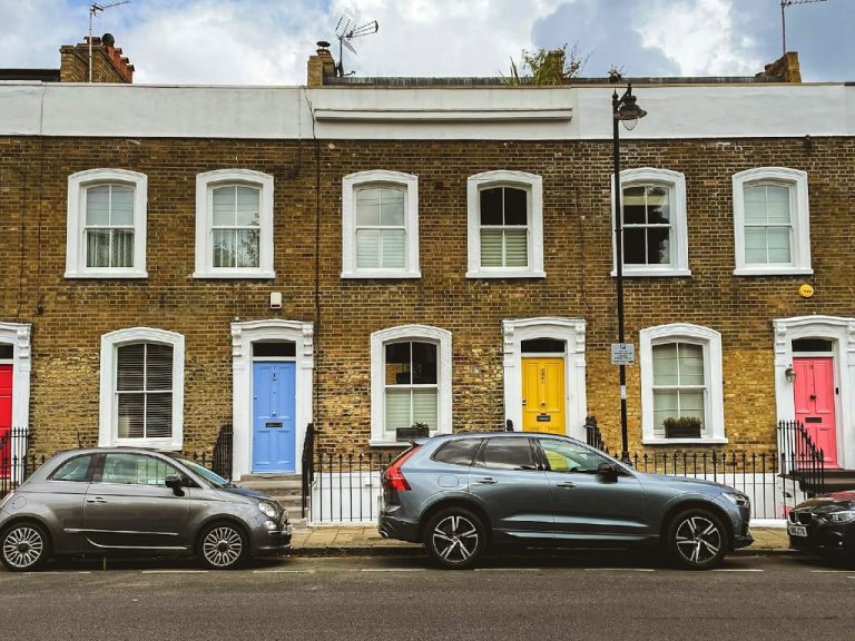 A row of Victorian houses, with colourful front doors, in London, UK, and with cars parked in the front.