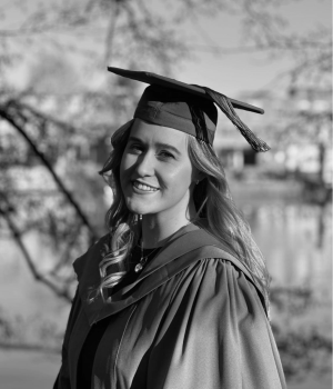 Tara Taylor-Deacon, proudly donning her graduation cap and gown, smiles radiantly as she stands outdoors.